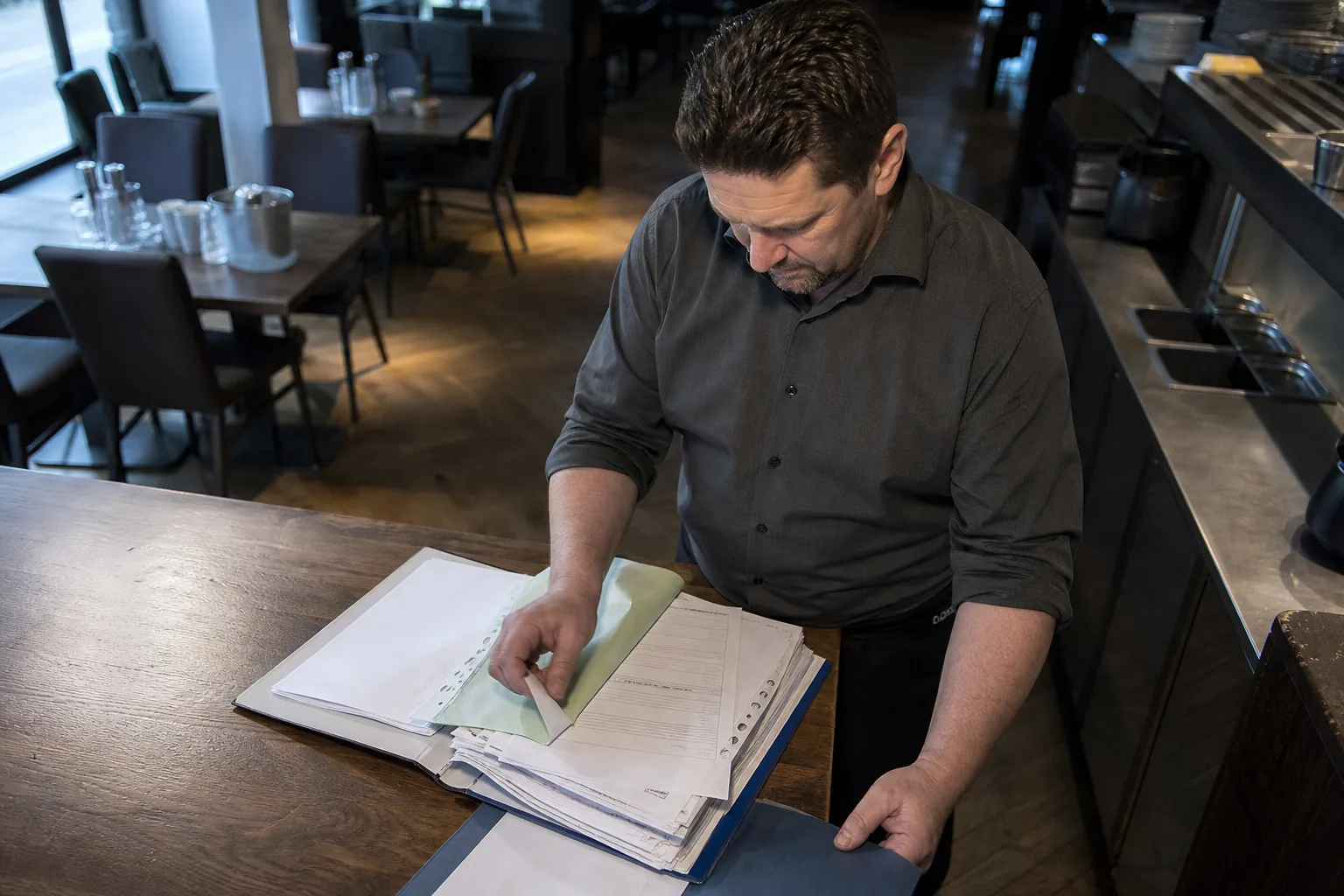 Restaurantleiter prüft unübersichtlich abgelegte Unterlagen in einem Personalordner.