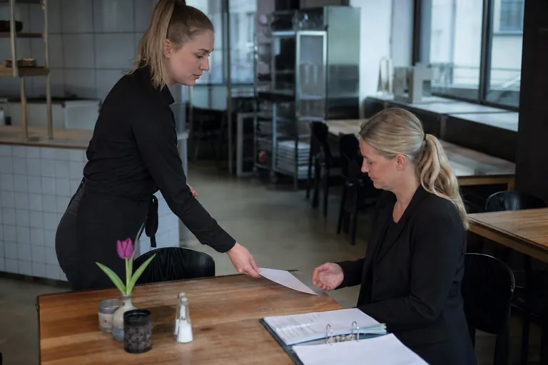 Neue Mitarbeiterin übergibt einer Personalverantwortlichen eine Bescheinigung in einem Restaurant.